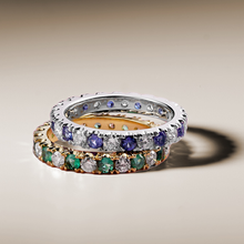 Load image into Gallery viewer, Two rings stacked on top of each other. On the bottom, the &#39;Always&#39; ring, a 18K yellow gold ring featuring a seamless blend of 0.65tcw round cut emeralds and 0.72tcw diamonds in prong settings. On top, a similar ring, in silver.
