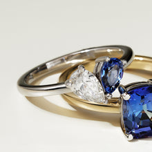 Load image into Gallery viewer, Two rings stacked on top of each other. The top, an elegant two stone ring in 14K white gold, featuring a 0.56ct Chatham sapphire and a 0.45ct lab diamond pear shape, VS/F, in a 3-prong setting, handcrafted in Montreal by Ex Aurum. Below it, another sapphire ring set in yellow gold.
