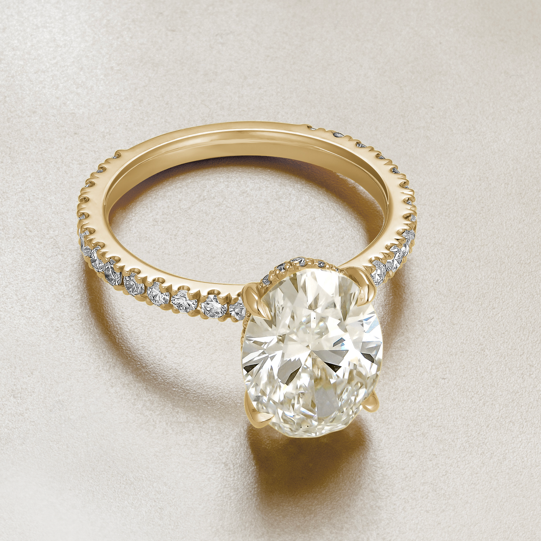 Luxurious engagement ring in 18K yellow gold, featuring a 3.09ct oval lab diamond (VS1 H) with a hidden pavé diamond halo and 0.55tcw of small round diamonds along the band, offering a blend of simplicity and detailed elegance.