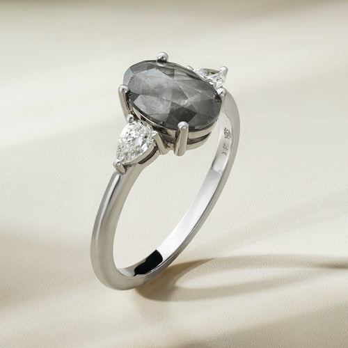  This unique engagement ring combines traditional and modern elements, featuring a 1.59ct oval salt & pepper diamond from the grey diamond family. It's accented by two pear-shaped diamonds totaling 0.32ct each, set in 18K white gold.
