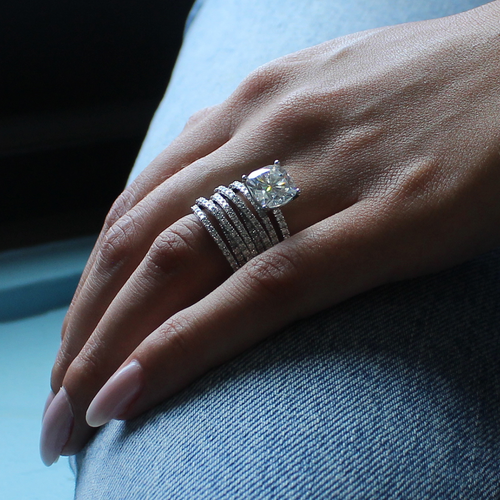 Model wearing our Destiny solitaire with other pavé bands. The Destiny is an exquisite engagement ring in 18K white gold, featuring a 3.18ct cushion cut diamond in a four-claw setting, complemented by 0.23tcw of small pavé set diamonds on the band, crafted to harmonize with various band styles.