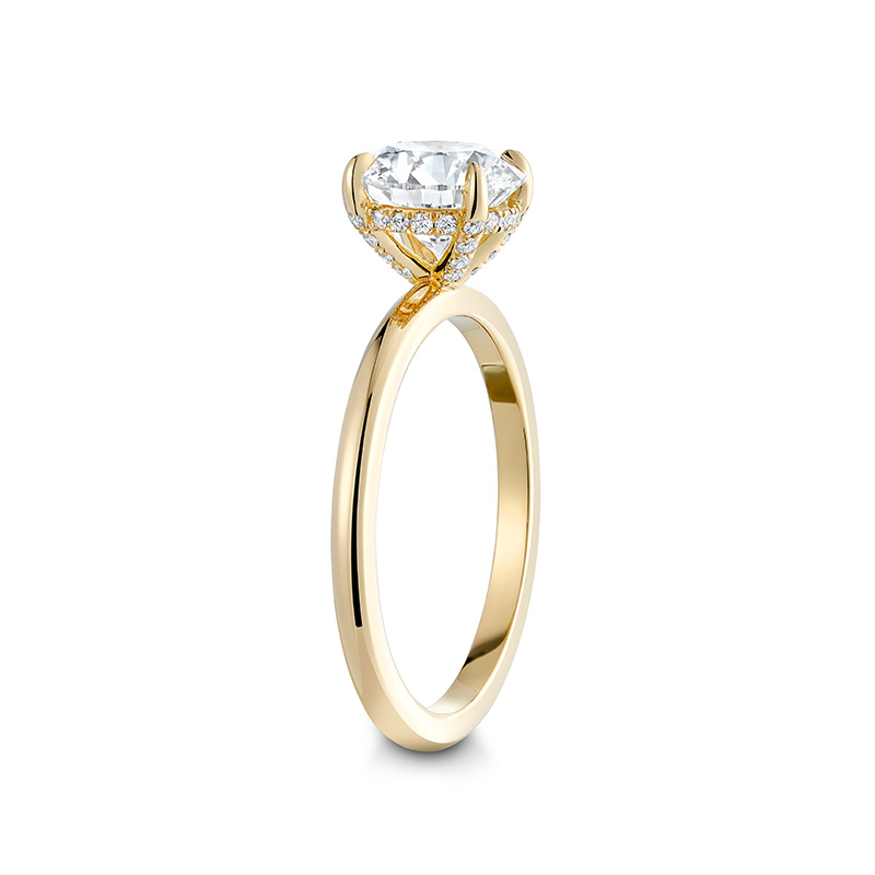 Charming engagement ring in 18K yellow gold, featuring a 1.5ct round brilliant diamond in an eagle claw setting, accented with a hidden halo of small diamonds.