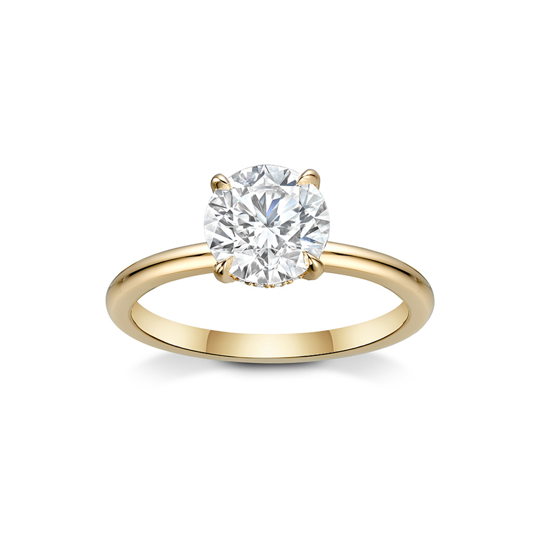 Charming engagement ring in 18K yellow gold, featuring a 1.5ct round brilliant diamond in an eagle claw setting, accented with a hidden halo of small diamonds.