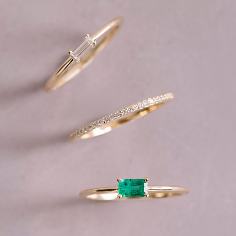 Emerald Burt ring with other stacking rings. 14K yellow gold, featuring a 0.25ct baguette-cut emerald in a low and long claw setting, slim and vibrant, ideal for unique stacking arrangements.